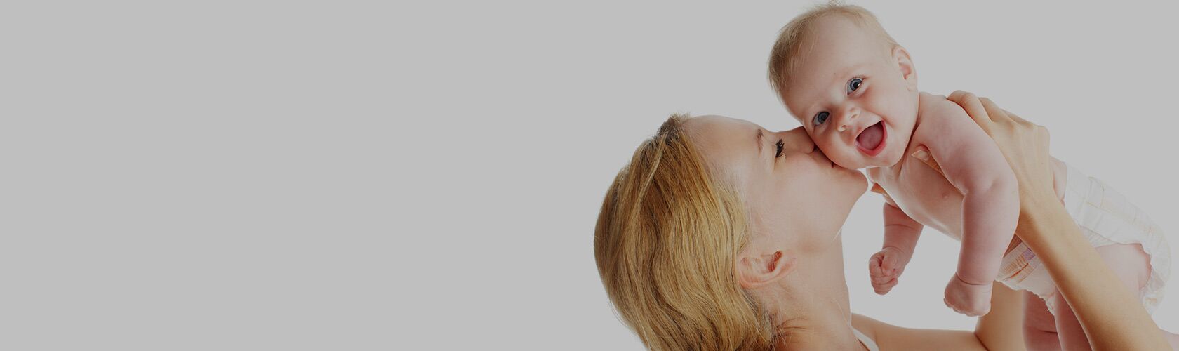 Eine Mutter hält ihr lachendes Baby liebevoll in die Luft und küsst es auf die Wange.