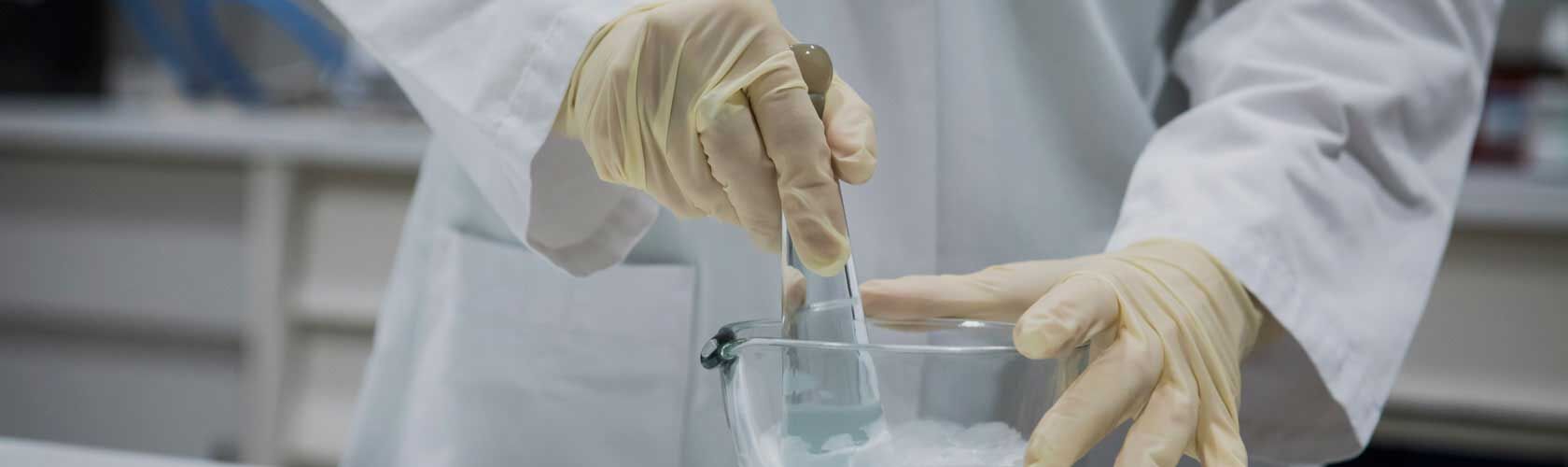 Ein Apotheker in weißen Handschuhen mischt Zutaten in einer Schüssel, um Qualität in der Jagdfeld Apotheke sicherzustellen.