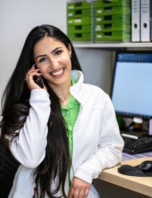 Eine lächelnde Frau telefoniert im Backoffice, während sie vor einem Computer sitzt.